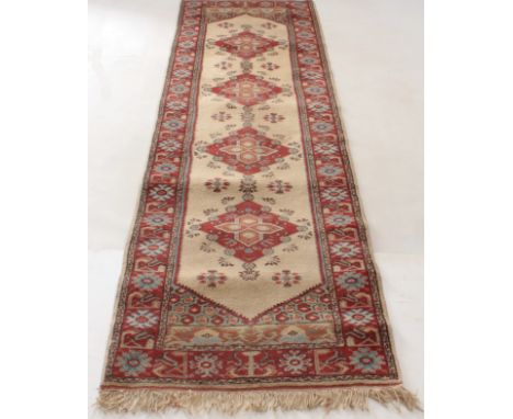 A Kazak wool runner - second half 20th century, with four brick red lozenge medallions on an ivory field, within a brick red 