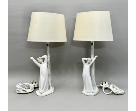 A pair of Nao porcelain figural table lamps - depicting sleepy children standing beside tree trunks, printed factory marks, w