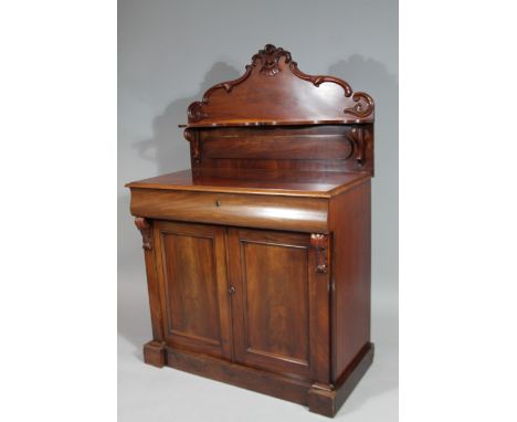 A Victorian mahogany chiffonier, the carved scroll back raised above a serpentine shelf, the subsection set with a cushion dr