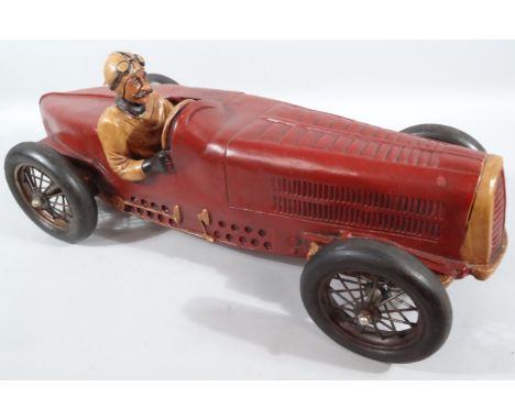 A 20thC carved wooden and metal model, of a vintage sports car, possibly an Alfa Romeo, the driver with raised goggles, with 