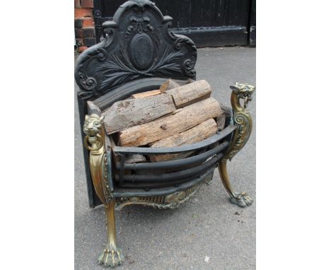 A rococo style metal and brass coloured fire grate, with shaped scroll back centred by an oval with bead outline surmounted b