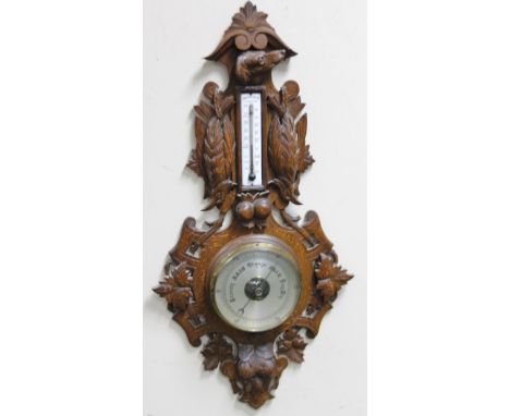 An early 20thC Black Forest style oak barometer and thermometer, the 15cm dia. dial surmounted by an enamel style thermometer