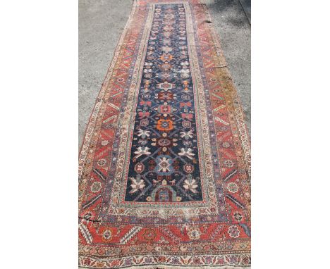 An early 20thC Middle Eastern carpet runner, in a repeat geometric floral pattern, predominately in red and blue. (380cm x 11