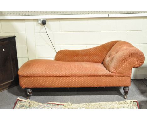 A Victorian chaise longue, with button back scroll side and back, upholstered in red fabric with fan pattern, on turned feet 