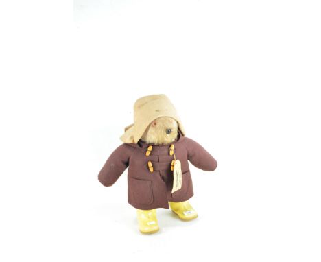 A vintage Paddington Bear, dressed in a characteristic felt hat, brown coat, yellow rubber Dunlop boots and travel ticket, he