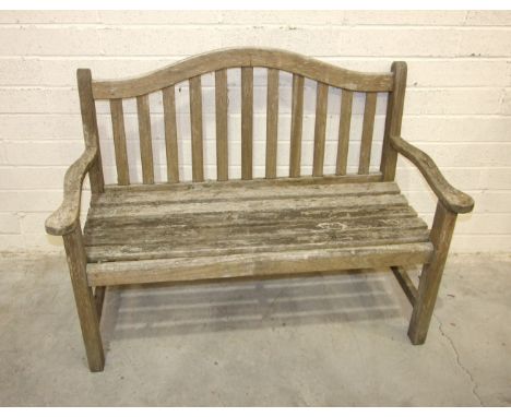 A teak garden bench with arched back and outswept arms, 130cm wide.