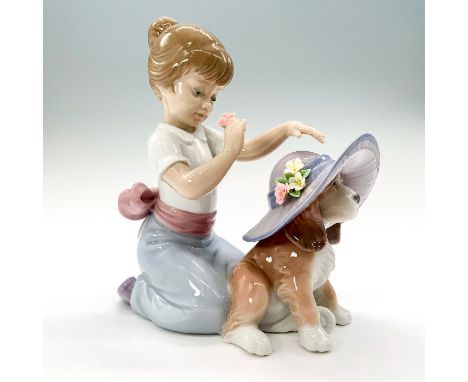 A figurine depicting a young girl dressed in a white shirt and blue skirt dressing her dog with a purple hat. Lladro backstam