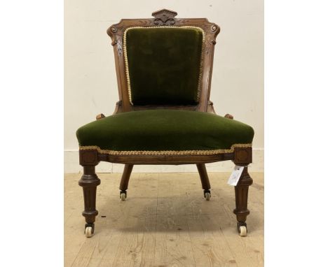 An Aesthetic walnut slipper chair with floral carved crest rail above seat in green velvet on turn supports terminating on ce