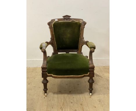 An Aesthetic period walnut open armchair, with floral carved crest rail above seat and arms in green velvet raised on turn su