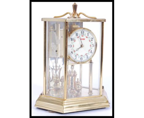 A 20th century brass anniversary clock with glass pane facia's enclosing an enamel faced dial by Kundo. Measures 25cm high.&n