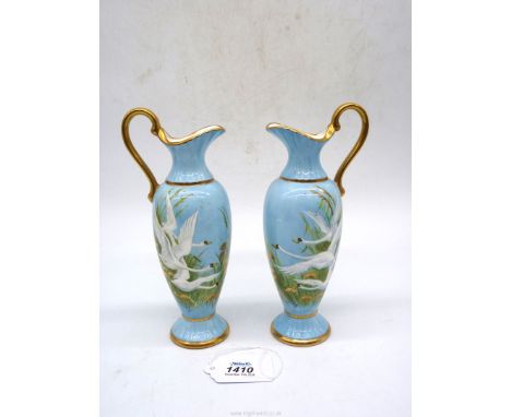A mirrored pair of hand painted Ewers decorated with swans flying through the grasses on blue backgrounds, both signed F. Cla