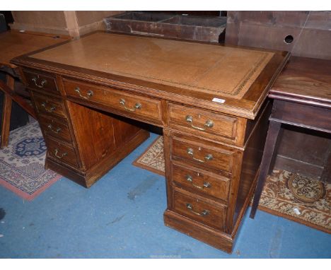 A compact Oak kneehole, double pedestal Desk having a gold tooled brown leather inset top, three frieze drawers and each pede