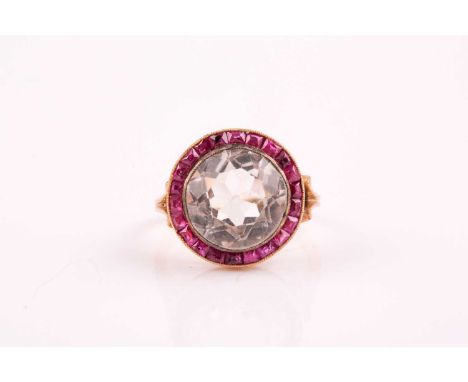 An early to mid 20th century yellow metal, ruby, and gemstone target ring, set with a pale quartz, within a calibre-set borde