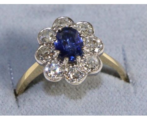 A Sapphire and Diamond Cluster Ring, an oval cut sapphire in a claw setting within a border of old cut diamonds in milgrain s