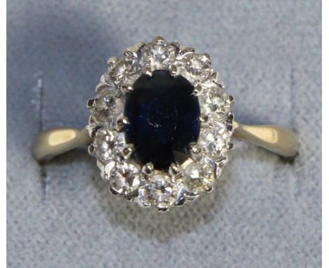 An 18 Carat Gold Sapphire and Diamond Cluster Ring, an oval cut sapphire in a claw setting, within a border of round brillian