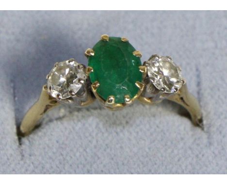 An Emerald and Diamond Three Stone Ring, an oval cut emerald between two round brilliant cut diamonds, in claw settings, to k