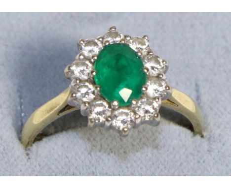 An 18 Carat Gold Emerald and Diamond Cluster Ring, an oval cut emerald within a border of round brilliant cut diamonds, in cl