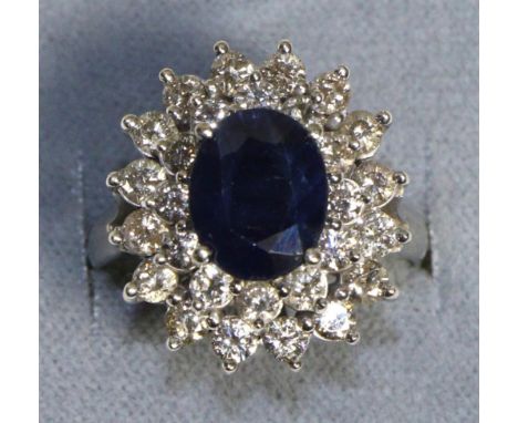 A 14 Carat White Gold Sapphire and Diamond Cluster Ring, an oval cut sapphire in a claw setting, within a two-tier border of 