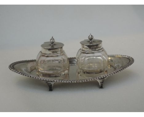 A silver ink stand of boat form having gadrooned rim and four bracket feet, containing two cut glass and silver ink wells, Bi
