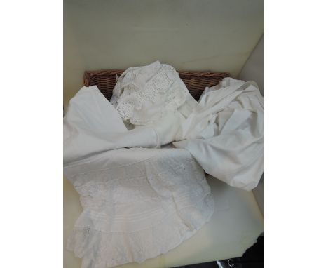 A wicker basket containing a selection of vintage linen including embroidered handkerchief pockets, lace doilies, tatting and