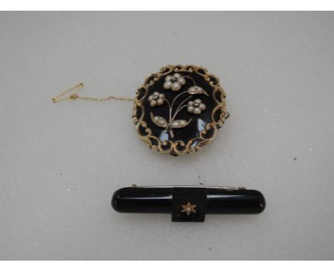 A yellow metal and black enamel mourning brooch having diamond and seed pearl floral decoration to front within a decorative 