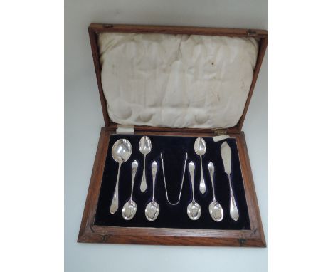 An oak case containing a set of six teaspoons with matching soup spoon, nips and butter knife, all of Arts and Crafts design,