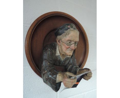 An early 20th century Austrian wall plaque having hardwood circular frame containing ceramic figure of old man reading