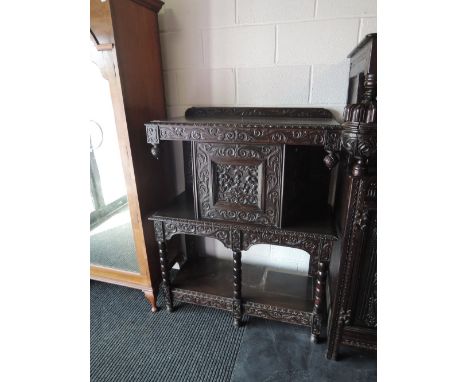 A late Victorian dark oak credenza having extensive foliate carved decoration with canted top cupboard over bobbin frame and 