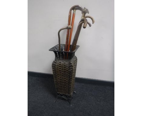 A metal wicker stick stand containing seven assorted walking sticks 