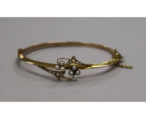 A cased Edwardian 9ct gold and seed pearl set hinged bangle.