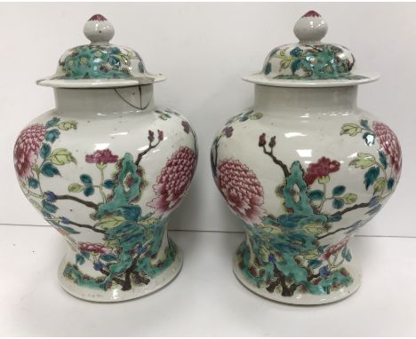 A pair of 19th Century Chinese famille rose vases and covers, the main body decorated with blossoming foliage raised on a sha