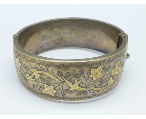 A silver bangle with gold applied decoration, with partly scratched off inscription