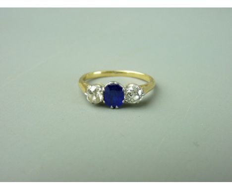 AN UNMARKED GOLD DRESS RING with blue oval central stone and two quarter carat flanking diamonds, 2.8 grms gross, size 'K'