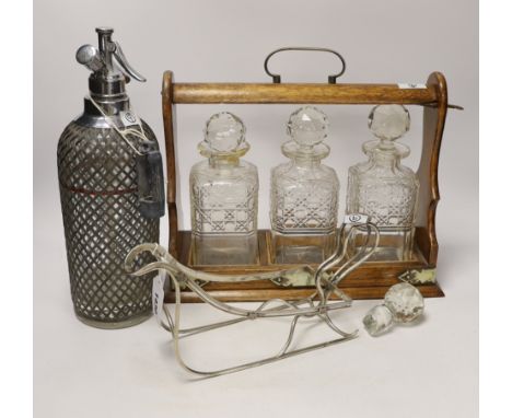 An oak three bottle tantalus, a German 800 standard white metal bottle cage and a vintage soda syphon, 36cm wide