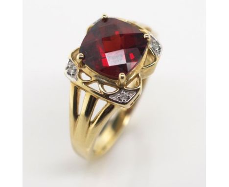 Garnet and diamond set 9ct yellow gold ring with a facetted cushion cut center stone, diamond shoulders and open work setting