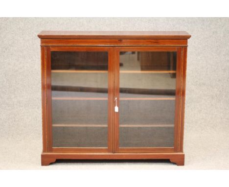 AN EDWARDIAN MAHOGANY BOOKCASE of shallow oblong form, crossbanded with stringing, moulded cornice over three glazed doors en