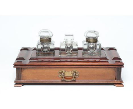 A LATE VICTORIAN MAHOGANY DESK STAND of of oblong form, the moulded edged top with dished pen rests centred by three large cu