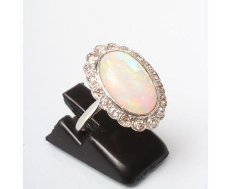 AN OPAL AND DIAMOND CLUSTER DRESS RING, the oval cabochon polished pale opal open back collet set to a border of eighteen bri