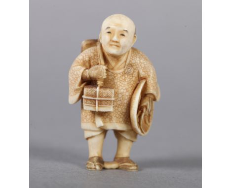 A LATE 19TH CENTURY JAPANESE IVORY NETSUKE, a man standing with his hat under his arm, carrying parcels  over his shoulder, s