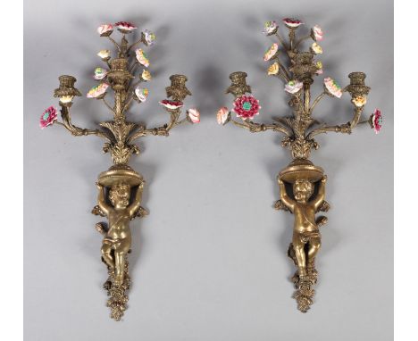 A PAIR OF BRASS AND PORCELAIN THREE LIGHT WALL SCONCES in the form of a cherub holding aloft four flowering branches, 20th ce