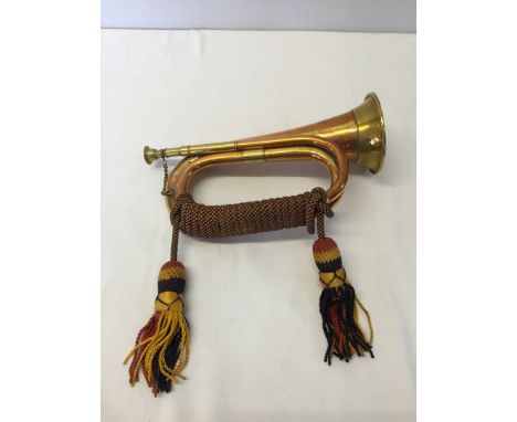 A brass bugle with blue, red and gold cords.