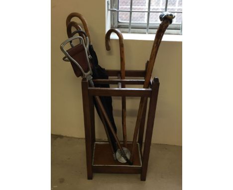 A vintage oak stick stand with 2 shooting sticks, a badger handled stick, 2 umbrellas and another stick.