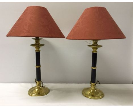 A pair of brass stick table lamps with rust coloured shades