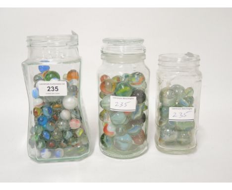 Three glass jars containing a collection of various marbles