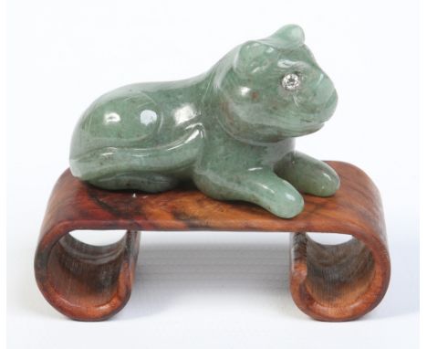 An antique Indian carved mottled jade model of a recumbent tiger with diamond inset eyes and raised on a scroll shaped wooden