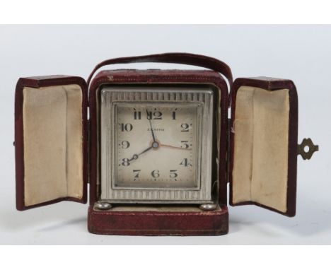 An Art Deco Zenith white metal travelling alarm clock in fitted leather case. With engine turned banded engraving, raised on 