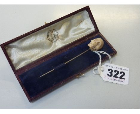 A STICK PIN, with carved skull within a fitted box