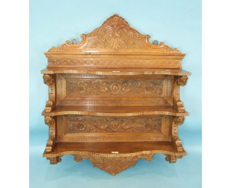 A 19th century Italian carved wall display shelf having three shaped serpentine shelves and profusely-carved back boards, 84c