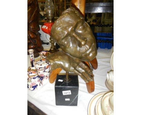 A bronze of a face and hand on a black marble base