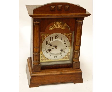 An early 20th century continental oak cased mantel clock having a brass arched dial with silvered chapter ring and Arabic num